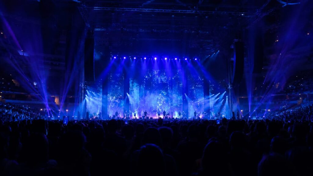 David Byrne концерт в Бангкоке — сцена концертного зала UOB LIVE с синей и фиолетовой подсветкой и силуэтами зрителей вечером